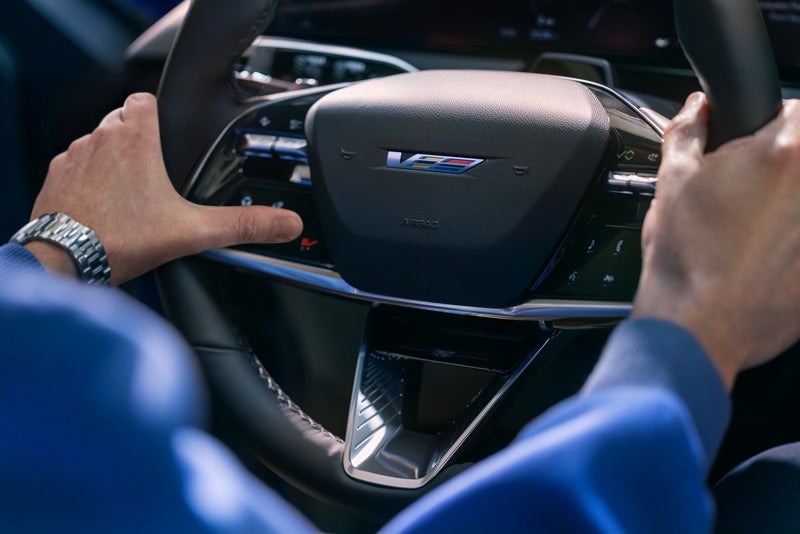 Close-up of a Man About to Press the V-Button on the 2026 OPTIQ-V Steering Wheel | Cadillac of Billings in Billings MT